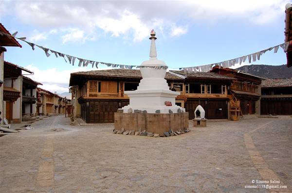White stupa on stone base in cobbled square among Tibetan wooden houses