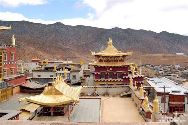 Golden roofs of Ganden Sumtseling monastery among brown mountains and white houses