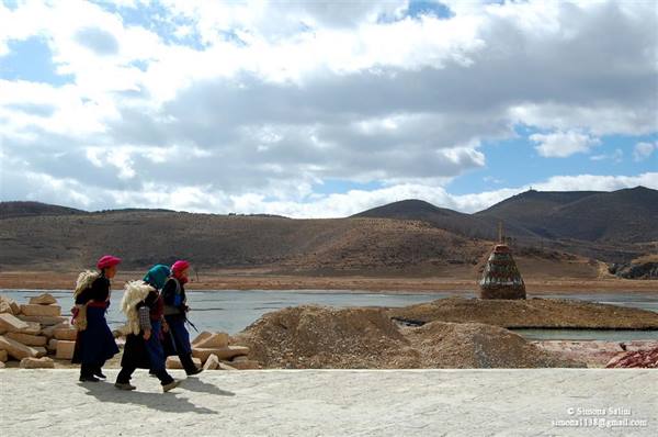 Three Tibetan women walk by a lake with a stone pile