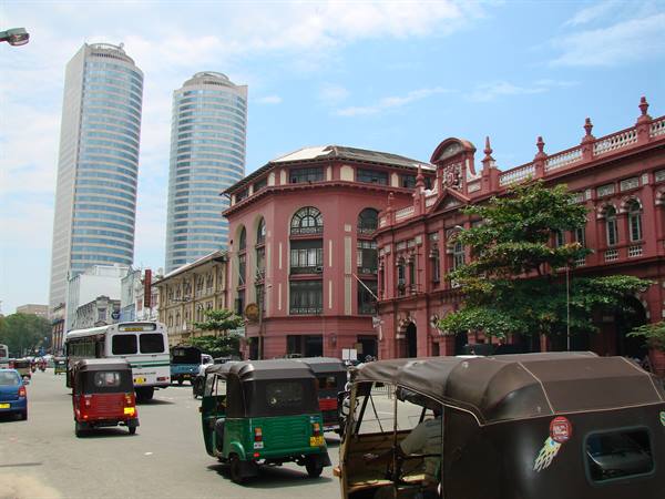 Tuk-tuks and buses in traffic past the red colonial building, Colombo