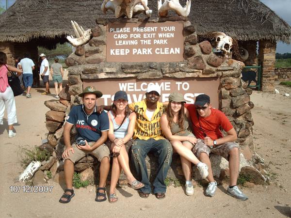 Five tourists sitting at the stone and thatch entrance of Tsavo East