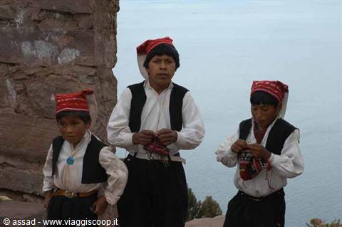 Boys in red caps knitting beside rock wall on Lake Titicaca, Taquile island