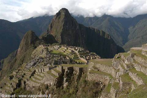 Machu Picchu stone ruins among green terraces and cloud-covered mountains