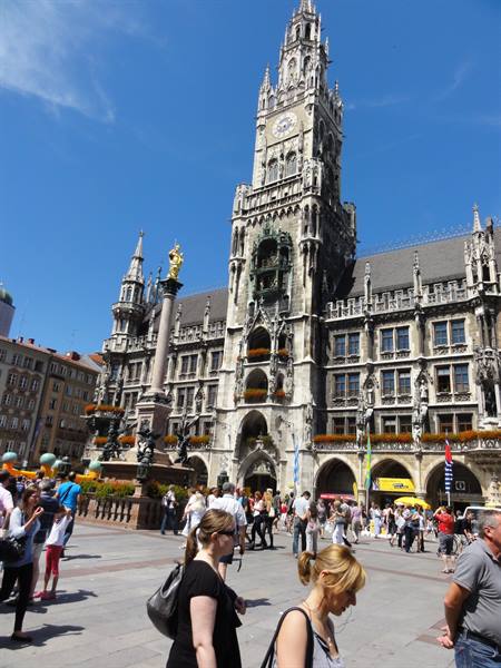 Tourists stroll past the Gothic Neues Rathaus under Munich's blue sky