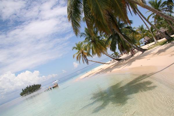 White sand beach with leaning palms, turquoise water, small pier and anchored boat