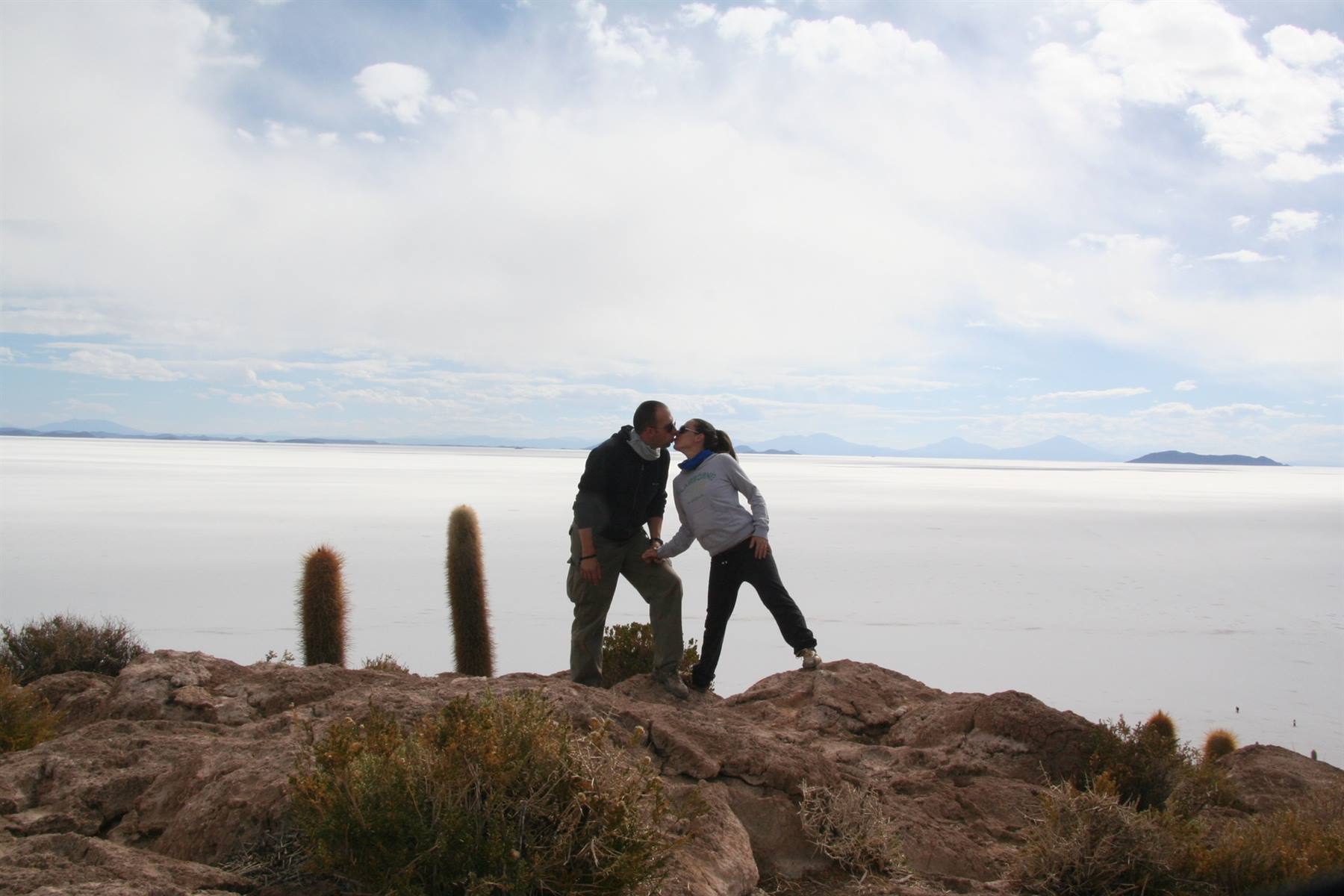 Coppia si bacia su roccia con cactus, Isla Incahuasi, salar bianco sotto