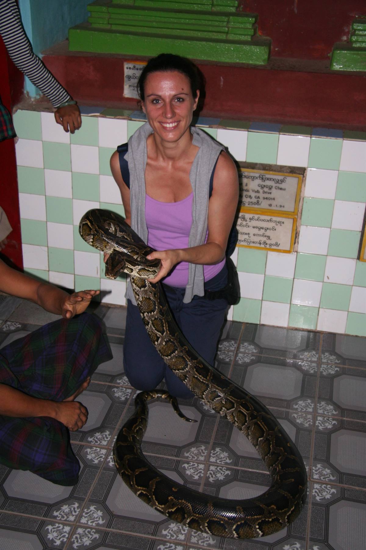 Donna sorride reggendo un grande pitone in un tempio piastrellato