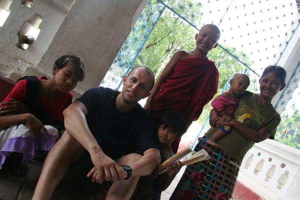 Tourist with young Buddhist novice in maroon robe and families under white pavilion