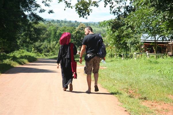Tourist with backpack and veiled woman walking on dirt road among trees