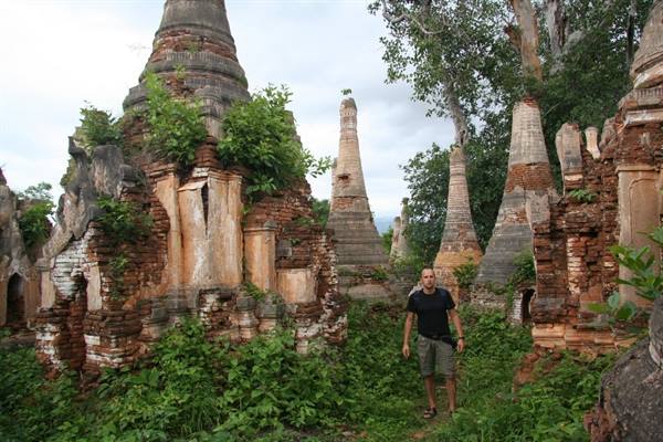 Man among crumbling brick stupas overgrown with vegetation at Shwe Inn Dein