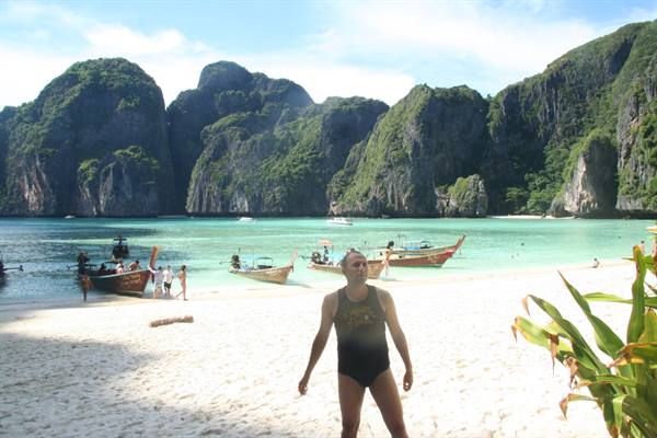 Tourist in swimsuit on Maya Bay beach, longtail boats moored by limestone cliffs
