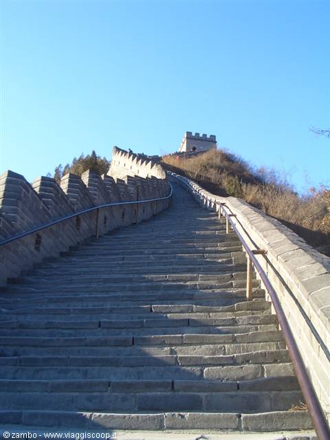 Steep stone staircase of the Great Wall climbs toward a watchtower under blue sky