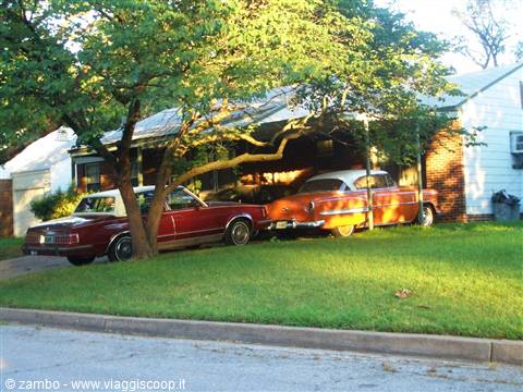 Two vintage cars parked in front of a brick house under a tree