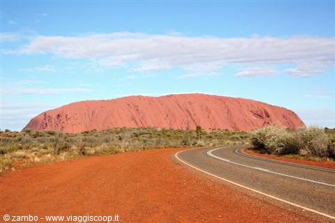Paved road through red sand with Uluru rock in the background