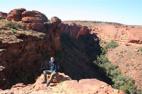 Man sitting on red sandstone rock at Kings Canyon among cliffs and green shrubs