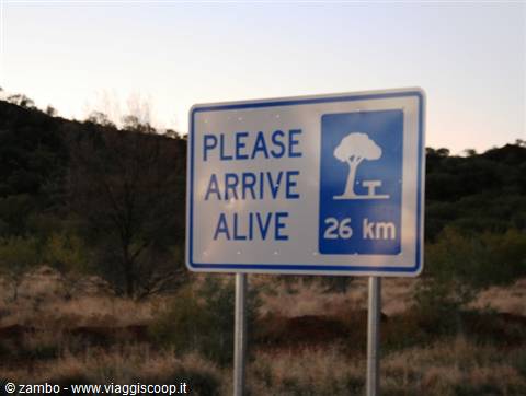 Blue 'Please arrive alive' road sign shows picnic area 26 km ahead