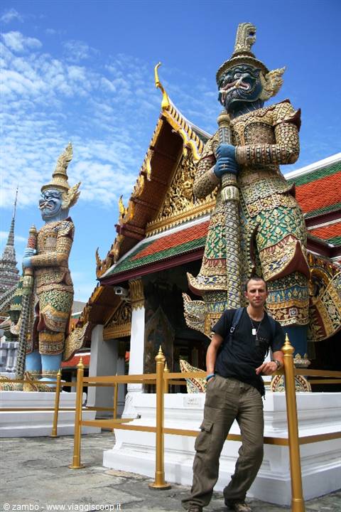 Tourist beside golden yak guardian statues at Wat Phra Kaew under sunny sky