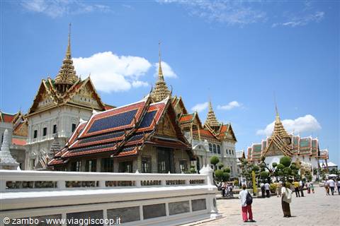 Tourists stroll through Bangkok's Grand Palace beneath golden spires and blue sky