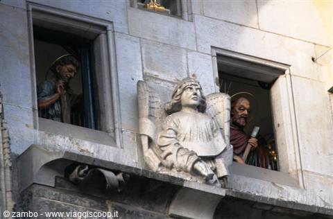 Wooden saint statues peering from windows of a marble facade