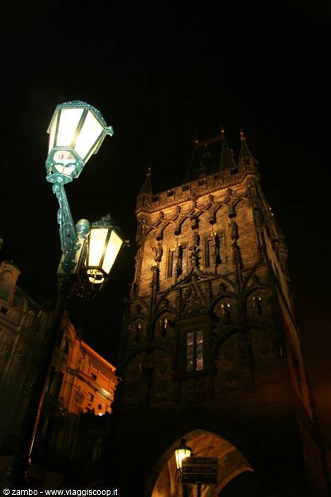 Green streetlamp glowing beside the Gothic Powder Tower at night in Prague