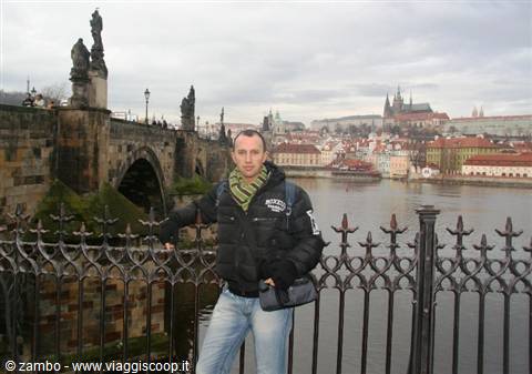 Tourist by Charles Bridge railing, Prague castle and Vltava river under cloudy sky