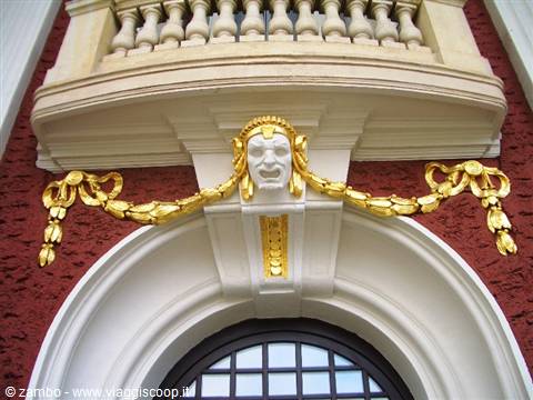 Golden theatrical mask and garlands on red facade, Riga theater