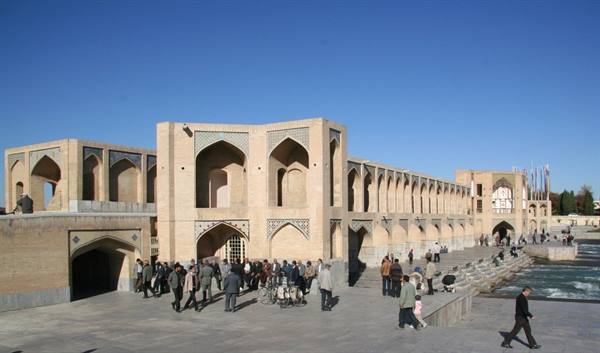 Visitors stroll along Khaju Bridge in Esfahan, brick arches under a clear blue sky