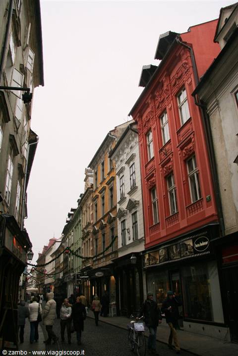 Pedestrians on cobbled street among colorful old buildings, looks like Ljubljana