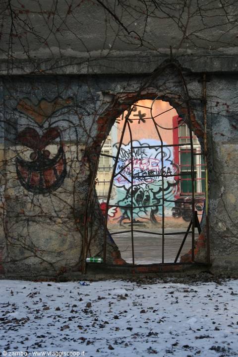 Cracked wall with rusty grille, colorful graffiti beyond, snow on the ground
