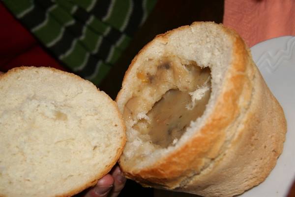 Hollowed bread bowl filled with hot soup, held in hand
