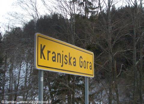Yellow road sign at Kranjska Gora entrance, bare trees and snow