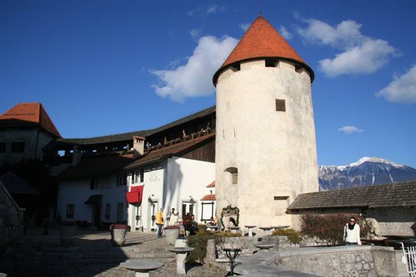 Tourists in Bled Castle courtyard, white round tower with red roof and snowy mountains