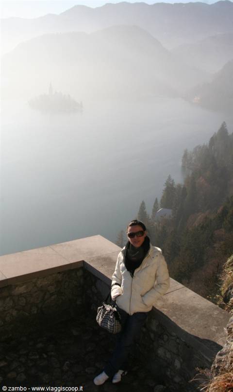 Tourist on castle stone wall, misty Lake Bled with island church