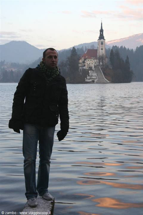 Tourist standing on a stone pillar at Lake Bled, island church behind