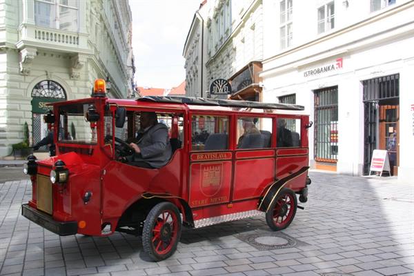 Red tourist shuttle bus with driver on cobblestones in Bratislava old town