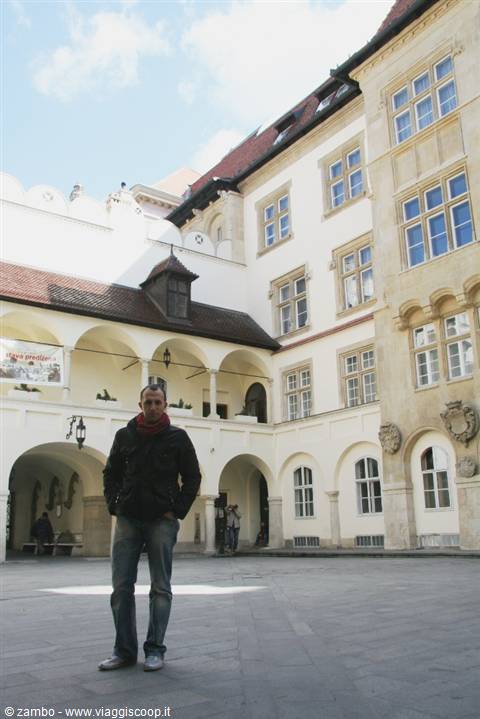 Man standing in the arcaded courtyard of Brno Old Town Hall, pale walls and arches