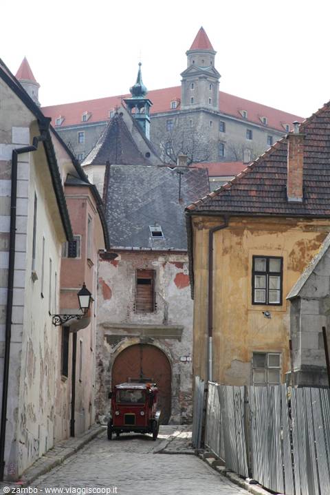 Cobbled alley with old red car, Bratislava Castle towering in the background