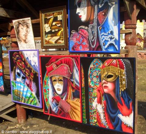 Velvet paintings of Venetian masks displayed at an outdoor market stall