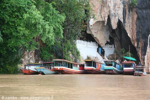 Longtail boats moored on muddy river beneath limestone cave entrance