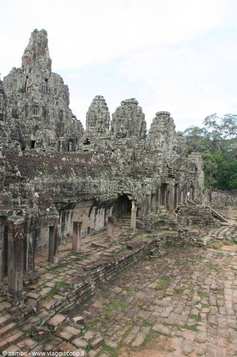Stone towers with carved faces at Bayon temple, Angkor, moss-covered ruins and paved courtyards