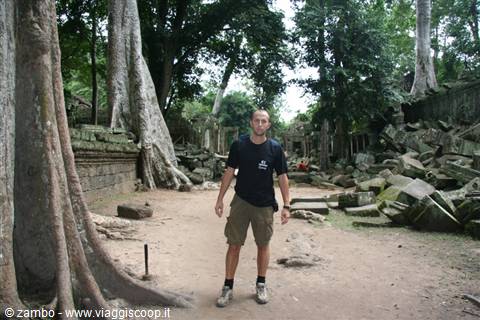 Tourist among giant tree roots and stone ruins at Ta Prohm