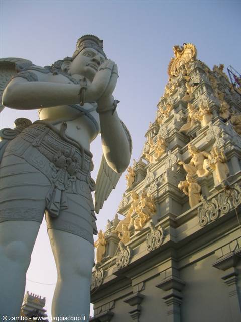 White Garuda praying statue beside the temple's carved golden gopuram