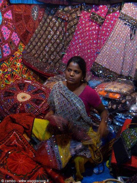 Woman in sari among colorful mirror-embroidered textiles at her market stall