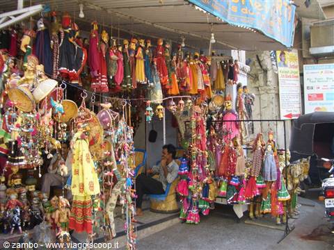 Colorful puppets hanging at a stall, vendor sitting in a shaded street