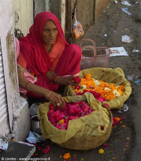 Woman in red sari selling rose and marigold petals from baskets