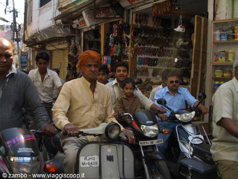 Man with orange dyed hair rides a scooter through busy bazaar traffic
