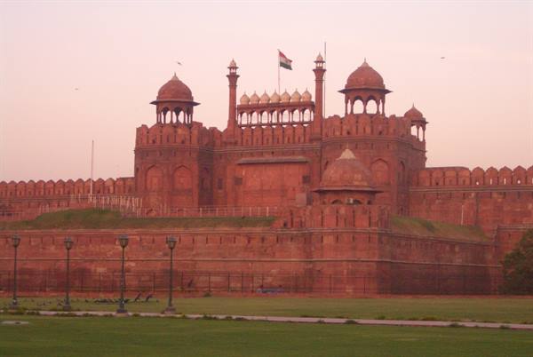 Delhi's Red Fort in sandstone under pink sky, Indian flag waving above