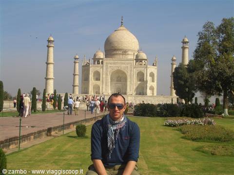 Tourist with sunglasses and scarf in front of the white marble Taj Mahal, green gardens