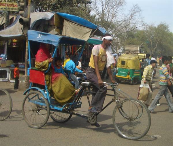 Cyclist carries passengers on a pedal rickshaw along a busy Indian street