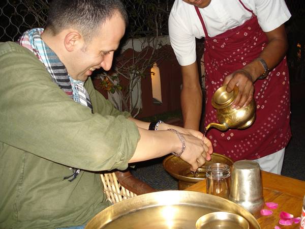 Waiter pours water from brass jug over guest's hands at table